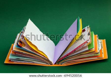A colorful, handmade junk journal on green background. Made from a recycled box and  random paper such as book pages, envelopes and wall paper. Blank pages are shown.