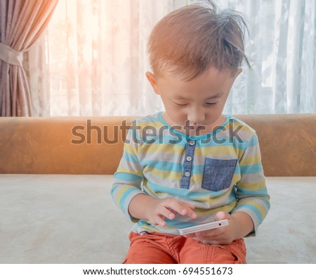 Little Asian boy playing a games in Smart phone on sofa in the room