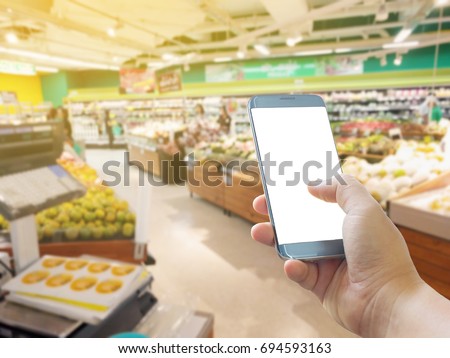Close up of hands holding cell telephone blank copy space screen. smart phone with technology concept. Abstract blur supermarket and retail store in shopping mall interior for background
