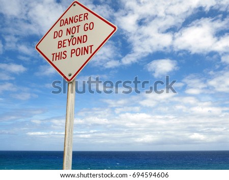 Danger sign with Pacific Ocean in background and blue sky with clouds. 