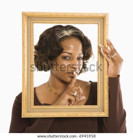 Woman holding frame around head holding finger up to lips.