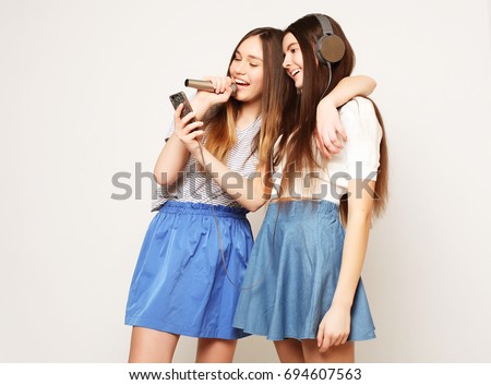 lifestyle, happiness, emotional and people concept: beauty hipster girls with a microphone singing and take picture with smartphone over white background