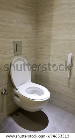 Hanging on wall White Open Toilet Bowl with beige ceramic tile walls and grey natural marble stone ground. Chrome flush button and telephone with tap on the wall.