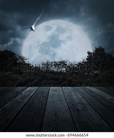 Old wooden table over tree, moon, bird and spooky cloudy sky, Horror background, Halloween concept