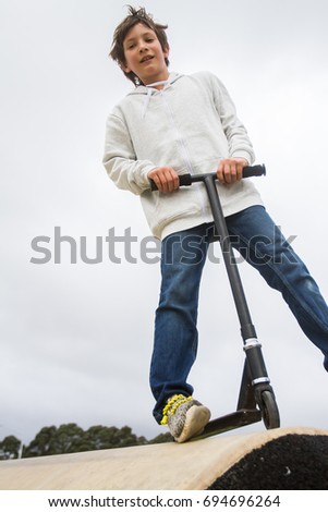 outdoor portrait of young teen boy riding a scooter on natural background