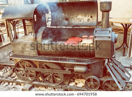 Barbecue grill with meat in shape of old steam locomotive. Bbq scene. Garden reastaurant. Yellow photo filter.