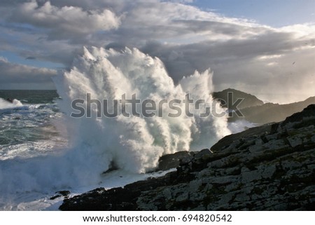 Giant Waves Nature Show crashing against dark colored cliffs, Meirás, A coruna, Galicia, Spain, raising a white foam dozens of meters against sky with stormy gray clouds in a dark green atlantic ocean