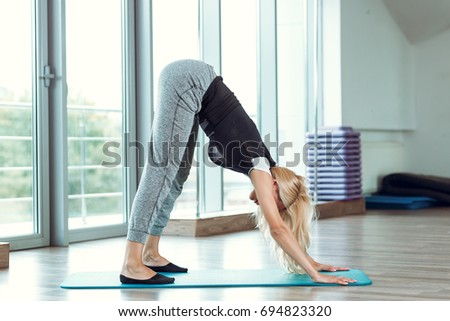 Young slender blond woman doing exercises in a light gym