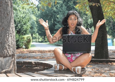 A young woman is sitting in the park with a laptop on her legs, strong emotions