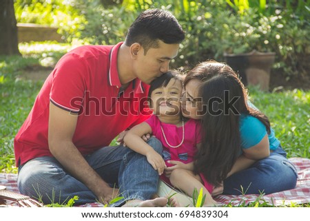 Daddy and mommy kissing their cute little daughter. Outdoors family portrait concept