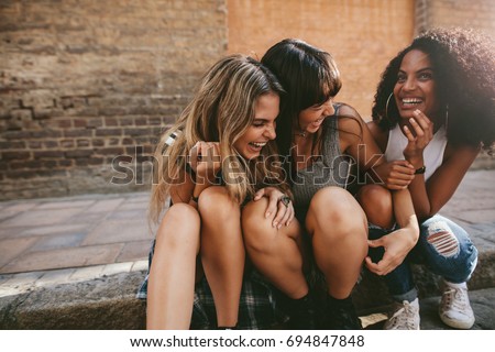 Group of young female friends hanging out in the city. Multiracial young women sitting by the street and having fun. Royalty-Free Stock Photo #694847848