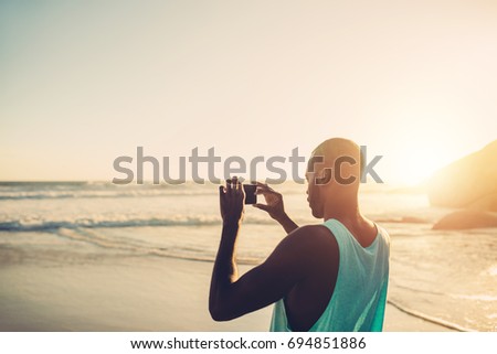 Afro american man taking photo of sea with mobile phone on the beach.