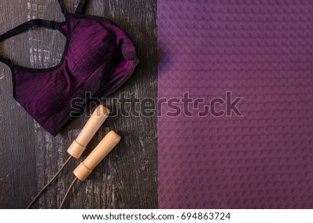 Closeup top view shot of sport bra and a jumping rope aside an exercise mat on a dark wooden floor background. Copy space