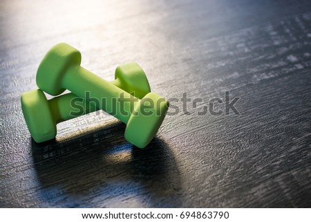 Closeup image of a pair of crossed green dumbbells on a dark wooden floor background. Copy space