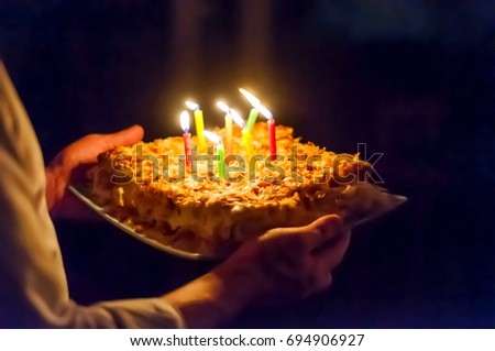 Person holding in his hands a Napoleon birthday cake with burning candles in the dark, surprise party stock image.