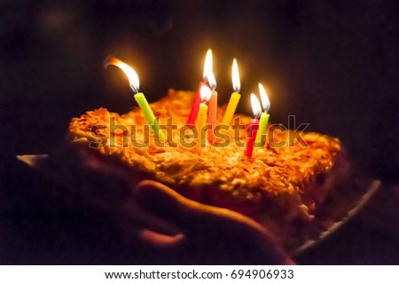 Person holding in his hands a Napoleon birthday cake with burning candles in the dark, surprise party stock image.