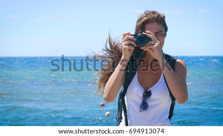 A female tourist photographer is taking pictures, with a backpack on her back, a wonderfully beautiful view of the blue sea and sky. Concept: travel, vacation, photo camera, photo courses, lifestyle.