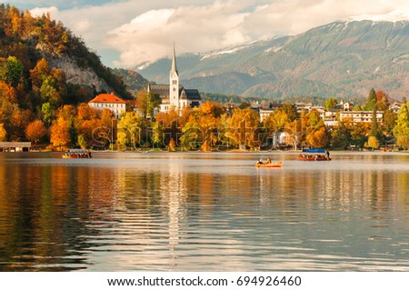 Amazing sunny autumn scenery of St. Martin's Church and Bled town with reflection in the lake and the Julian Alps on background. Location place: Bled Lake, Slovenia. Royalty-Free Stock Photo #694926460