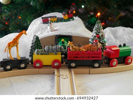 Christmas display featuring generic wooden train set, plastic, African animal toys, fake snow and a Christmas tree in the background- eclectic Christmas display concept
