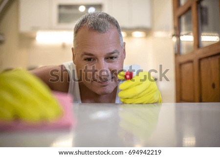 Attractive caucasian man cleaning the table in the kitchen. Man is doing some cleaning work in the house. Man's hand in yellow rubber glove with rag cleaning kitchen oven