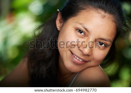 Headshot portrait of young hispanic woman on blurred natural background