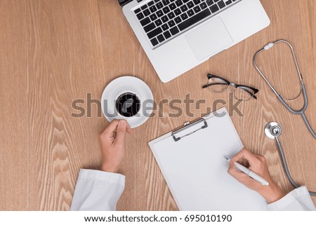 Top view of adult doctor working with clipboard on his desk and holding pen