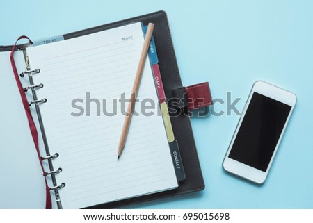 Creative flat lay style workspace desk with notebook, smartphone and pencil on modern blue background