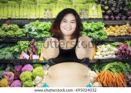 Picture of overweight woman showing thumbs up while standing in the vegetable store