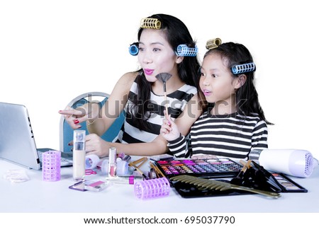 Asian woman looking at the computer laptop while doing makeup with her daughter, isolated on white background