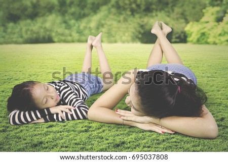 Picture of young mother relaxing with her daughter while lying down in the meadow