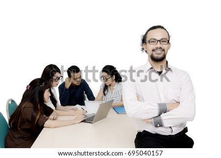 Portrait of a young male business leader folded hands while his team discussing on the background
