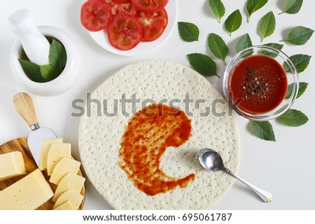 Top view of classic Italian pizza on a light background. Ingredients for pizza dough, basil, tomatoes, cheese, tomato sauce, spices.