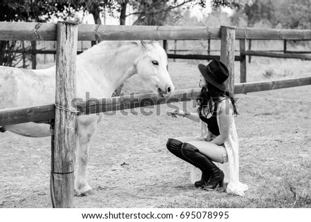 Sweet pretty woman on a rancho near beautiful horses farm posing at camera and have fun, curly brunette girl in american country style 