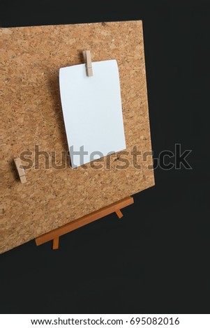 Cork board with mini clothespins magnet and a blank paper note on black background