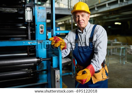 Portrait of senior factory worker smiling looking at camera standing by machine in modern industrial workshop Royalty-Free Stock Photo #695122018