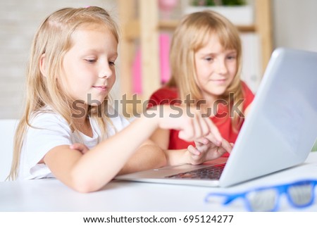 Portrait of pretty little girl using laptop while sitting at table with her elder sister, interior of lovely bedroom on background