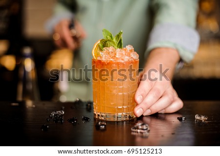 Bartender finished decorating his cocktail with mint and orange slice Royalty-Free Stock Photo #695125213