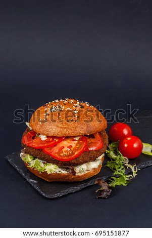 Craft beef burger with tomatoes on black table isolated on black background.
