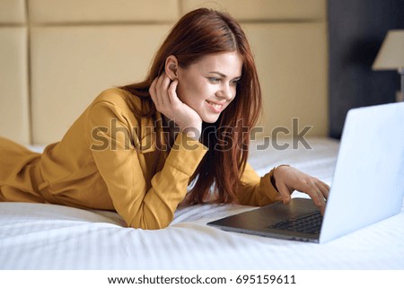 Woman smiling and working behind laptop lying in bed                               