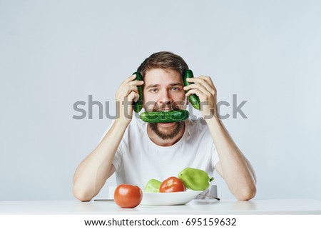 Vegan holds a cucumber in his mouth and at the head on a light background, a diet                               
