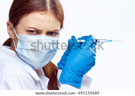 Woman doctor in a medical mask with a syringe on a light background portrait                               