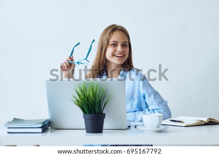Business woman smiling holding in her hand glasses working in the office behind a laptop                               