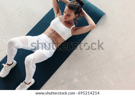 Young beautiful girl wearing fashion sports wear doing exercise on mat at loft gym, top view Royalty-Free Stock Photo #695214214