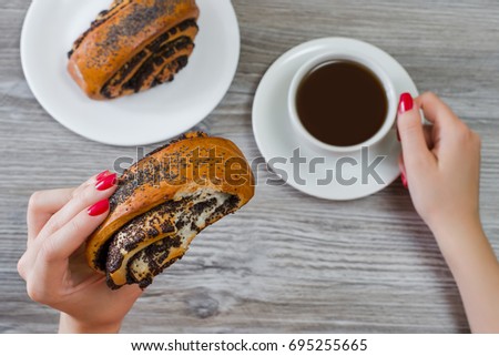 Bun with poppy seeds in woman's hand over table, cup of coffee on the background