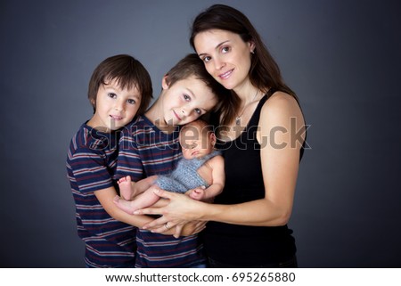 Family picture of three boys and their mom, kissing and hugging newborn baby at gray background, tender, care, love. Portrait of woman and children, happiness concept, isolated image