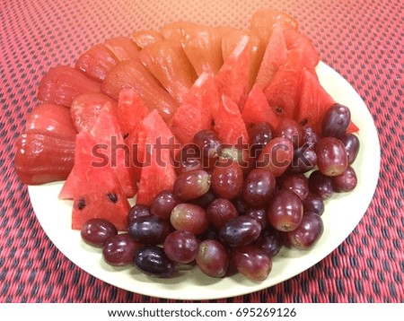 A lot of purple grapes, rose apple and slice of watermelon on white plate. Thai fruit.