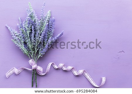 Lavender flower banded ribbon with bow on purple wooden background.