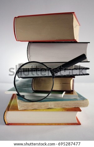 A stack of old and new books with a magnifying glass on a white background