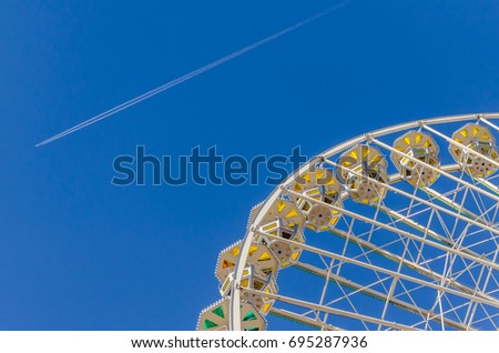  Ferris wheel with colored cabins against a clear blue sky at a funfair in Lyon against a clear blue sky at a funfair in Lyon while an plane is passing by Royalty-Free Stock Photo #695287936