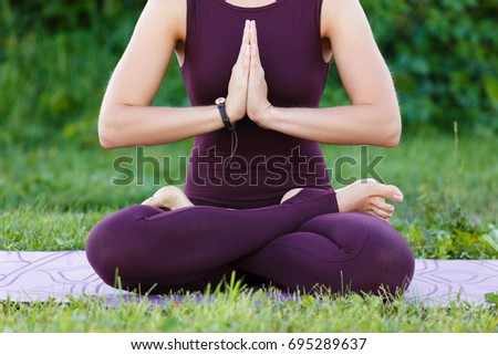 Young fitness woman practicing yoga lotus pose on the field with green grass, healthy lifestyle concept.